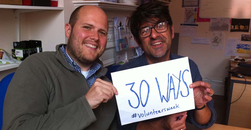 Two men hold a piece of card reading '30 Ways. #volunteersweek'.